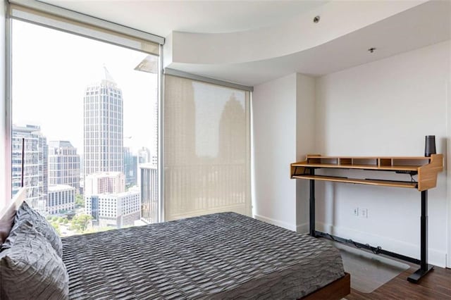 bedroom with a view of city, expansive windows, wood finished floors, and baseboards