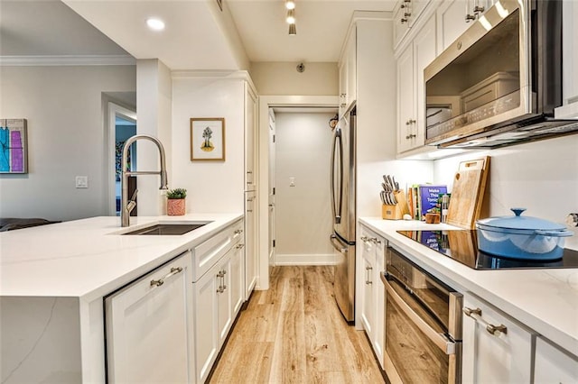 kitchen featuring ornamental molding, light wood-style floors, white cabinets, stainless steel appliances, and a sink