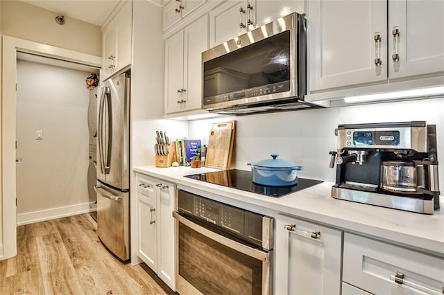 kitchen featuring decorative backsplash, light countertops, white cabinets, light wood-style floors, and appliances with stainless steel finishes