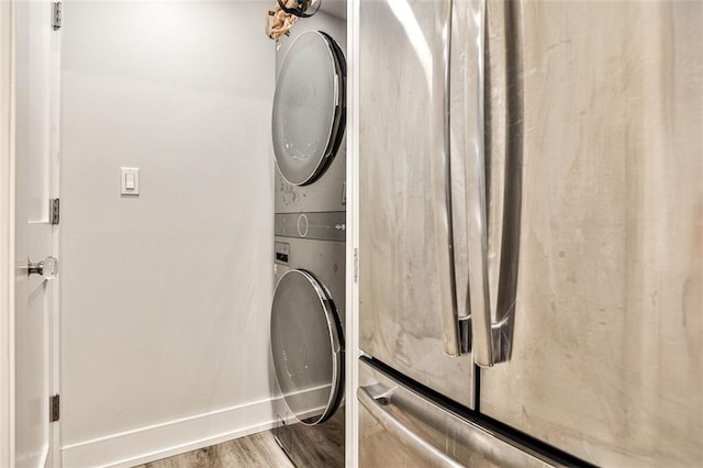 clothes washing area featuring laundry area, wood finished floors, baseboards, and stacked washer and dryer