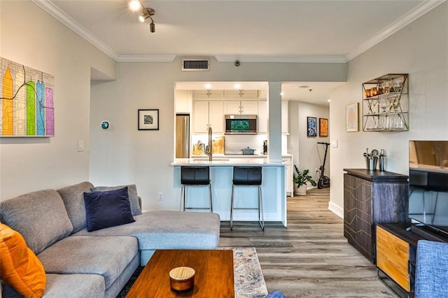 living area featuring visible vents, wood finished floors, baseboards, and ornamental molding