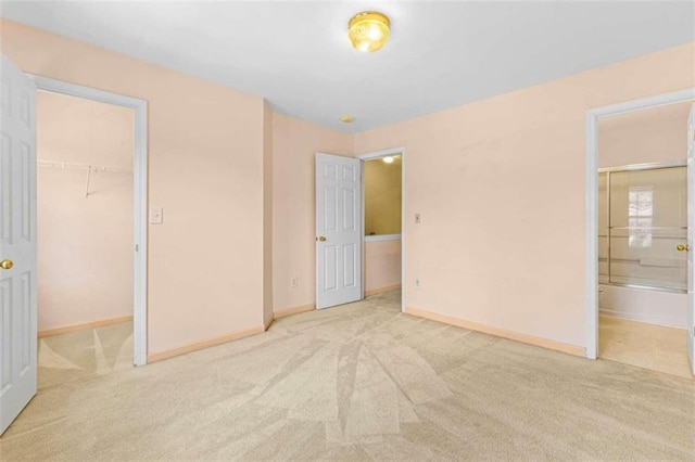 unfurnished bedroom with ensuite bath, a spacious closet, a closet, and light colored carpet