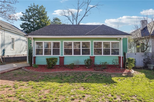 rear view of property featuring a shingled roof, a lawn, and fence