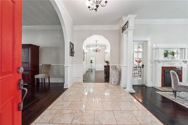 foyer with arched walkways, a wainscoted wall, ornamental molding, a brick fireplace, and a chandelier