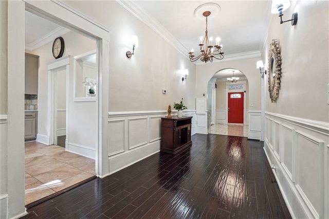 entryway with arched walkways, crown molding, wood finished floors, and a notable chandelier