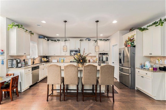 kitchen with stainless steel appliances, decorative light fixtures, white cabinets, a center island, and dark wood-type flooring