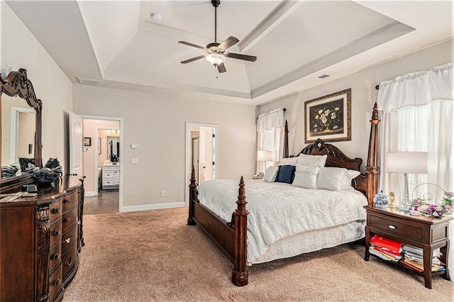 carpeted bedroom featuring ensuite bathroom, ceiling fan, and a tray ceiling