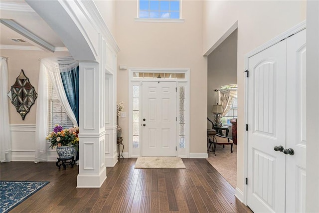 foyer featuring ornate columns, dark wood-type flooring, and crown molding