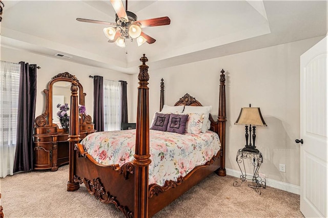 bedroom with light carpet, ceiling fan, and a raised ceiling