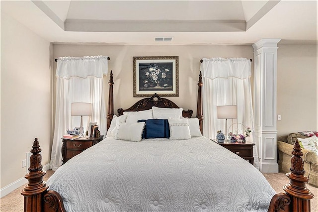 carpeted bedroom with ornate columns and a raised ceiling