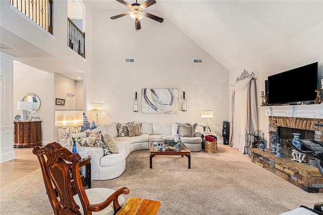 living room with high vaulted ceiling, a stone fireplace, light carpet, and ceiling fan