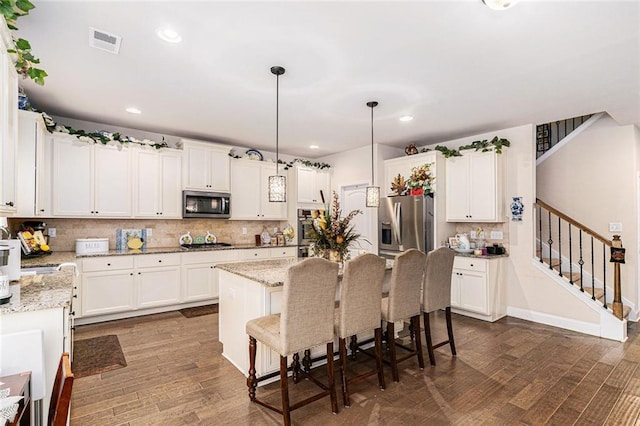 kitchen with appliances with stainless steel finishes, light stone countertops, a breakfast bar area, hanging light fixtures, and dark wood-type flooring