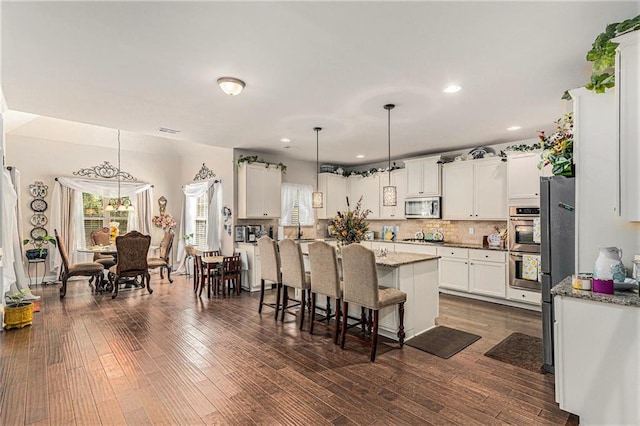 kitchen with dark wood-type flooring, white cabinets, light stone countertops, pendant lighting, and appliances with stainless steel finishes