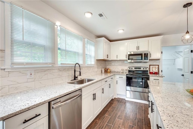 kitchen featuring pendant lighting, white cabinetry, sink, stainless steel appliances, and light stone countertops