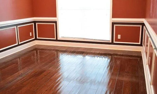 unfurnished room featuring a wainscoted wall, wood-type flooring, and a decorative wall