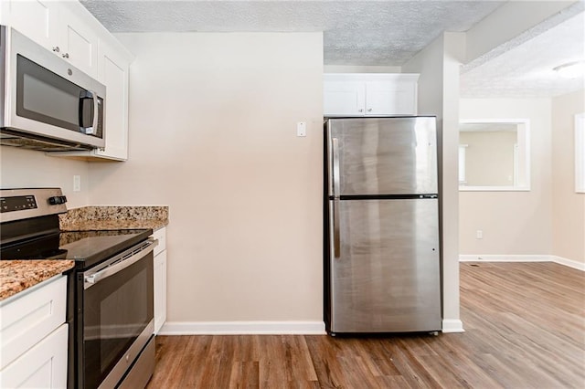 kitchen featuring a textured ceiling, light stone counters, white cabinetry, and stainless steel appliances