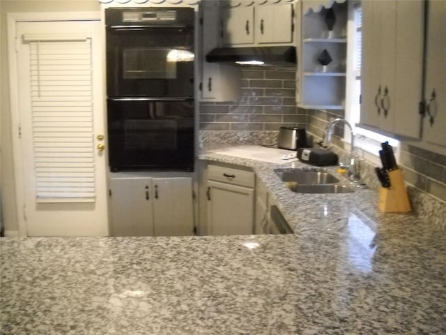 kitchen featuring black double oven, light stone countertops, sink, and decorative backsplash