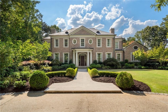 colonial inspired home with a front lawn, brick siding, and a chimney