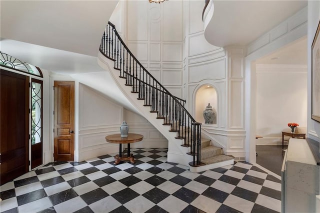 foyer entrance featuring stairs, crown molding, a decorative wall, and a towering ceiling