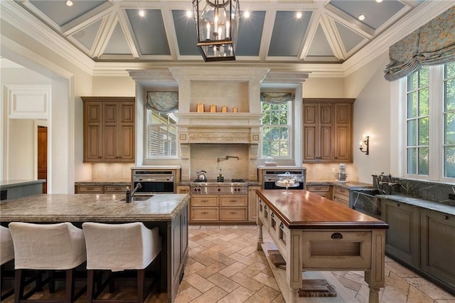 kitchen featuring crown molding, tasteful backsplash, a center island with sink, and coffered ceiling