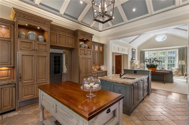 kitchen featuring an inviting chandelier, butcher block counters, an island with sink, and beamed ceiling