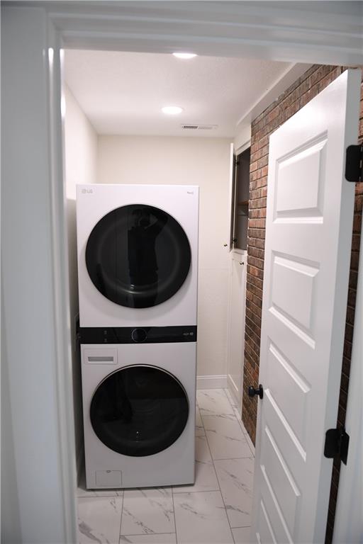 446 Brown Bridge Rd, Chatsworth, GA 30705 - laundry room with stacked washing machine and dryer, light marble finish flooring, and brick wall