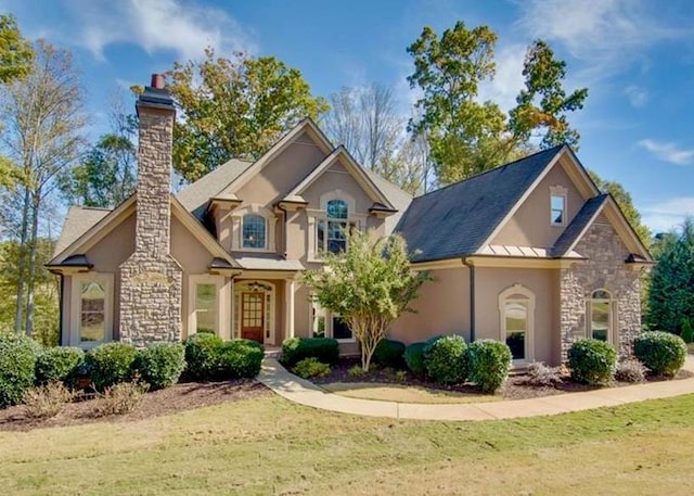 view of front of house with stone siding, a chimney, stucco siding, and a front lawn