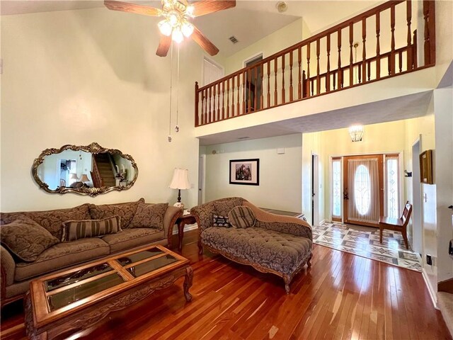 living room with hardwood / wood-style flooring, a towering ceiling, and ceiling fan