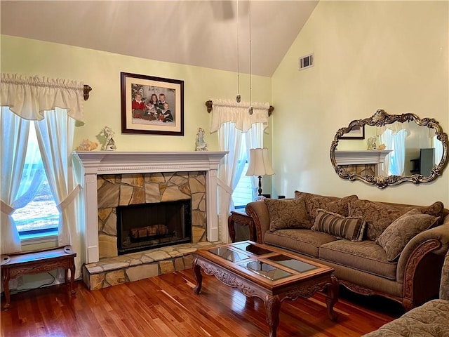 living room with wood-type flooring, a stone fireplace, and high vaulted ceiling