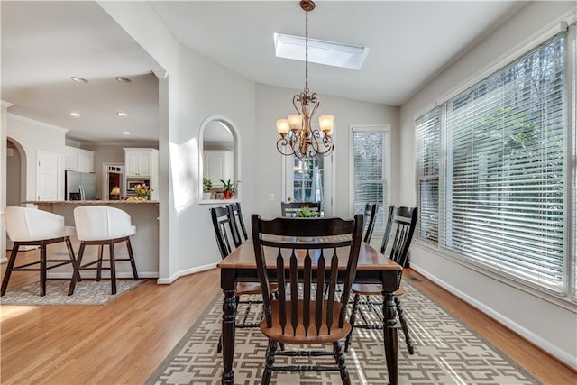 dining room featuring ornamental molding, vaulted ceiling with skylight, a chandelier, and light hardwood / wood-style floors