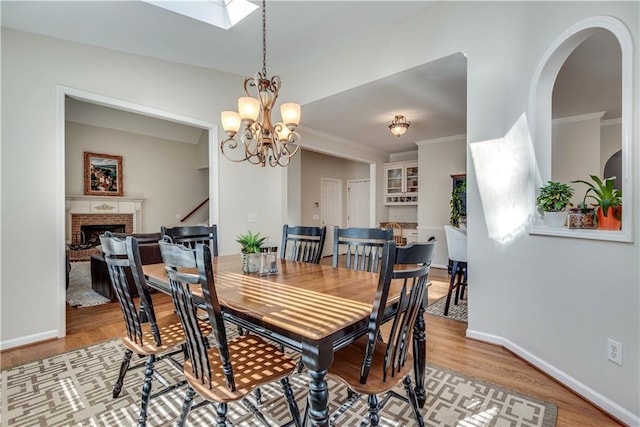 dining area with a skylight, light hardwood / wood-style floors, a chandelier, crown molding, and a fireplace