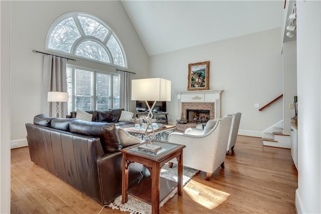 living room with high vaulted ceiling, a brick fireplace, and light hardwood / wood-style flooring