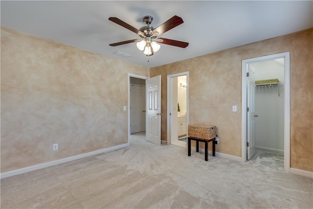 unfurnished bedroom featuring connected bathroom, ceiling fan, a walk in closet, and light colored carpet