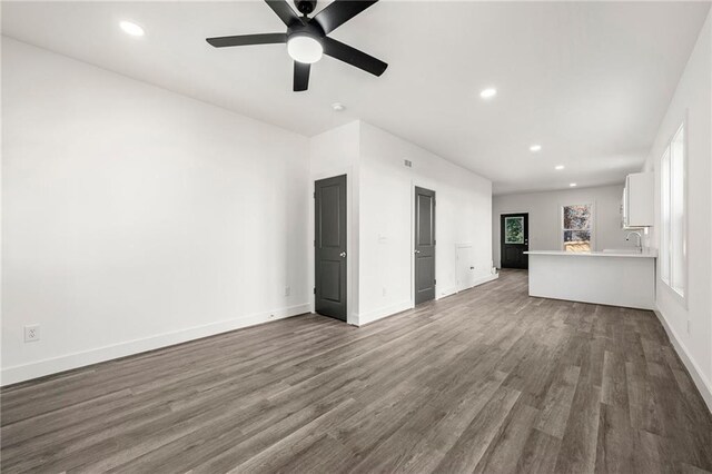 unfurnished living room featuring recessed lighting, baseboards, dark wood-style flooring, and a sink