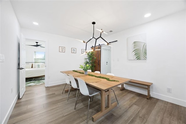 dining space with ceiling fan with notable chandelier and hardwood / wood-style flooring