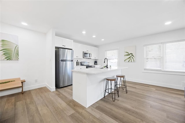 kitchen with a center island with sink, sink, a kitchen bar, white cabinetry, and stainless steel appliances