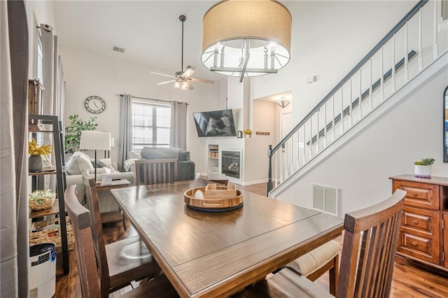 dining space featuring stairs, wood finished floors, a ceiling fan, and visible vents