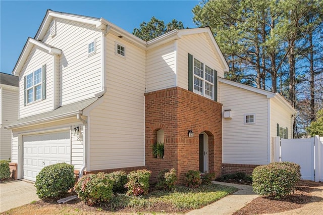 view of front of house with driveway, brick siding, an attached garage, and fence