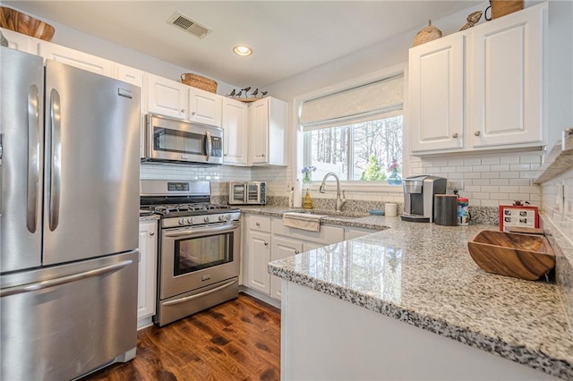 kitchen with dark wood-style floors, visible vents, appliances with stainless steel finishes, white cabinetry, and backsplash