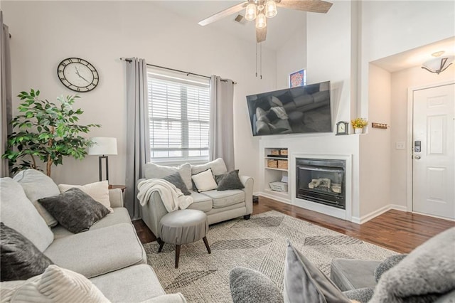 living room featuring wood finished floors, baseboards, high vaulted ceiling, ceiling fan, and a glass covered fireplace