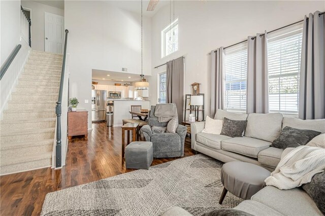 living area featuring a wealth of natural light, stairs, dark wood-type flooring, and a towering ceiling