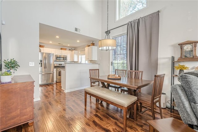 dining area featuring visible vents, a healthy amount of sunlight, a high ceiling, and hardwood / wood-style flooring