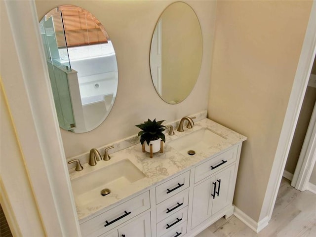 bathroom with double vanity, baseboards, a sink, and wood finished floors