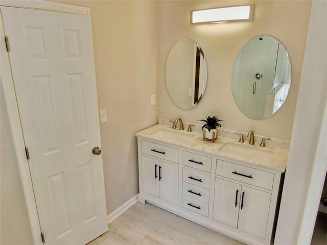 bathroom with double vanity, wood finished floors, a sink, and baseboards