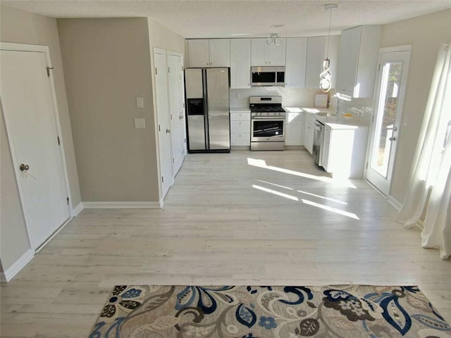 kitchen featuring white cabinetry, baseboards, light wood-style floors, light countertops, and appliances with stainless steel finishes