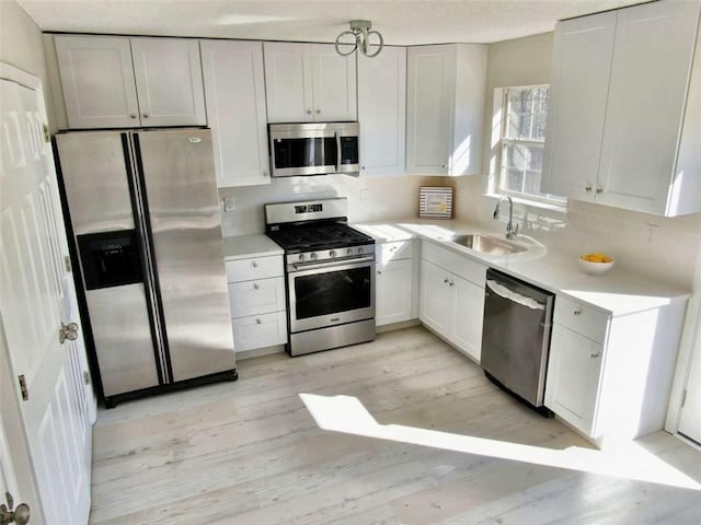 kitchen with light wood finished floors, stainless steel appliances, light countertops, backsplash, and a sink