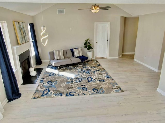 living room featuring lofted ceiling, a fireplace, wood finished floors, visible vents, and a ceiling fan