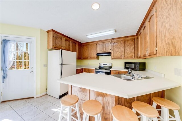 kitchen with black microwave, a peninsula, a sink, stainless steel electric range, and freestanding refrigerator