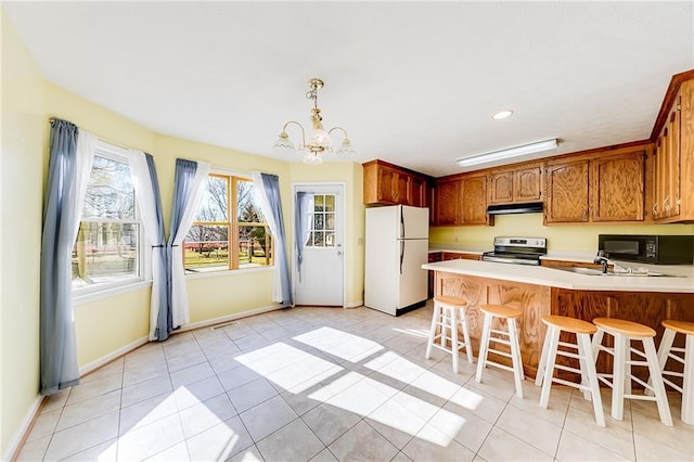 kitchen with black microwave, under cabinet range hood, a peninsula, freestanding refrigerator, and stainless steel range with electric stovetop