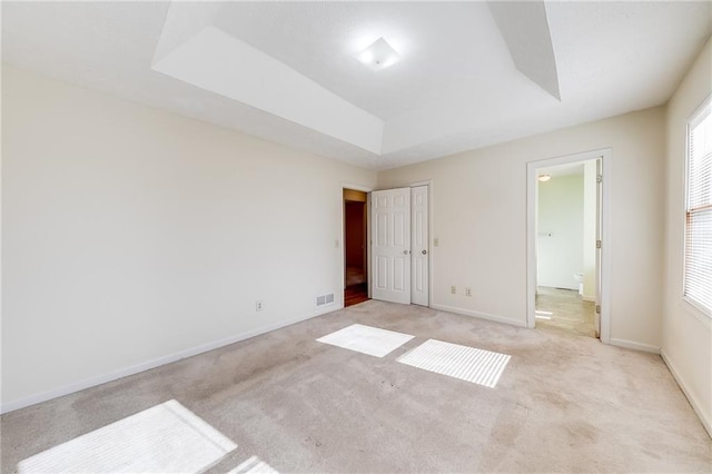 unfurnished bedroom with a raised ceiling, light colored carpet, and baseboards